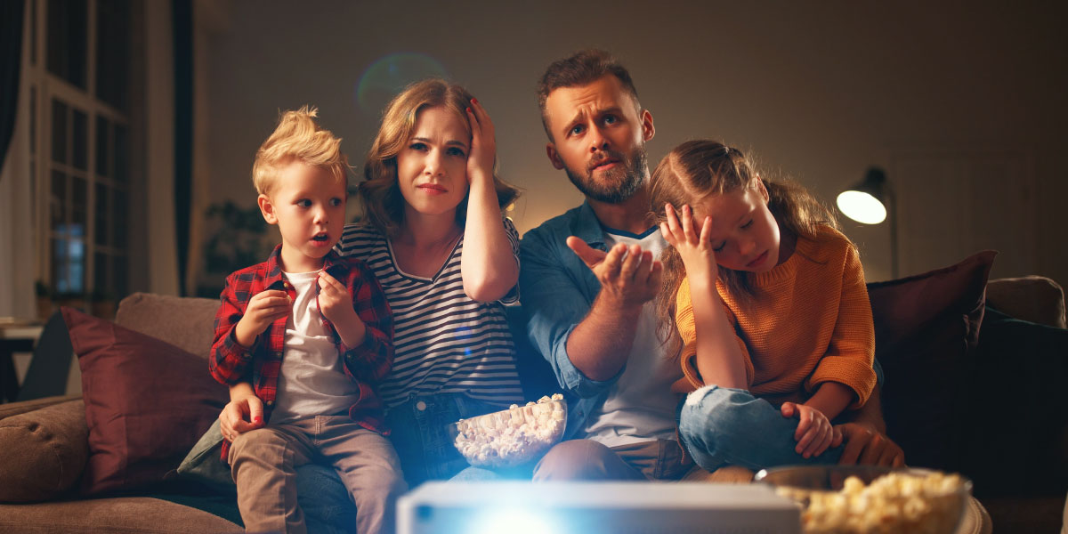 Young family watching tv with shocked faces