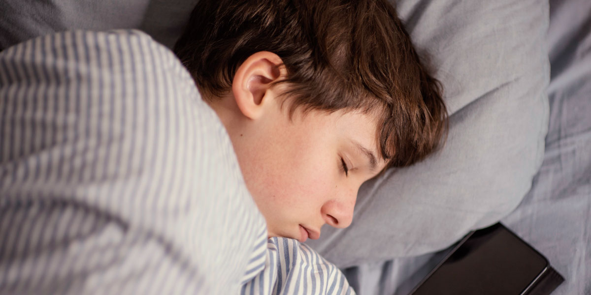 Boy asleep with mobile beside