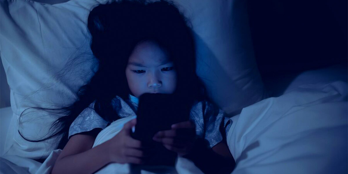 Girl with blue screen light whiles on bed