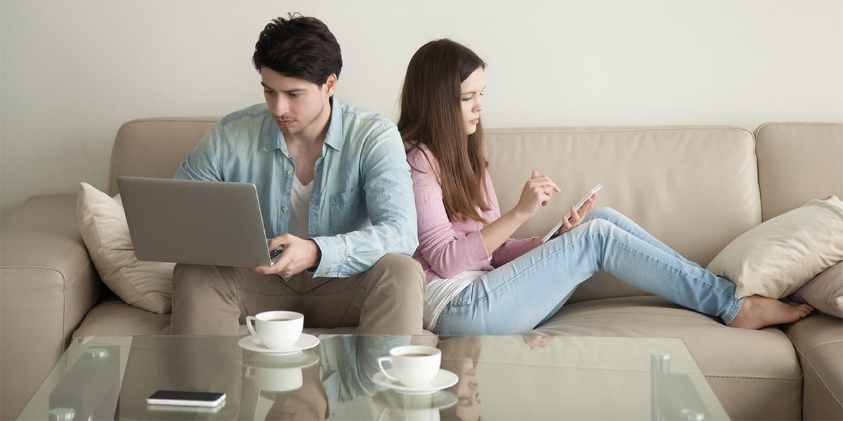 two teenagers sitting in their living room using the internet on phone and laptop.