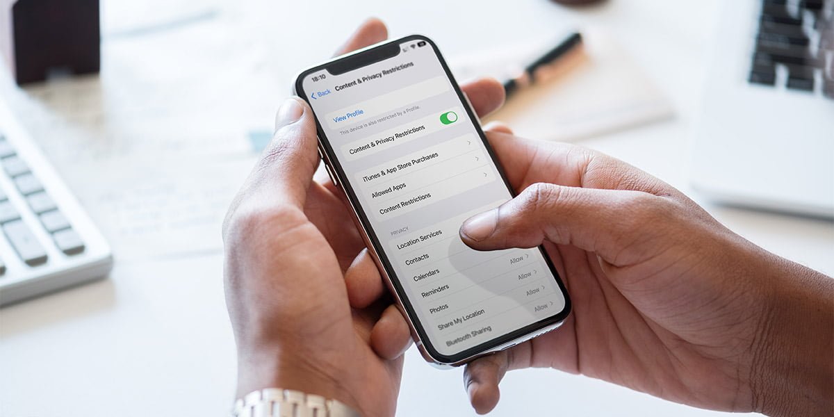 A set of hands holding an iPhone that shows the Content & Privacy Restrictions page