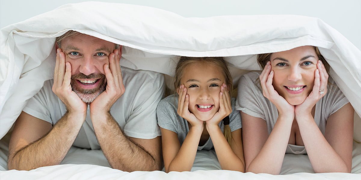 Parents and young girl smiling under a blanket.