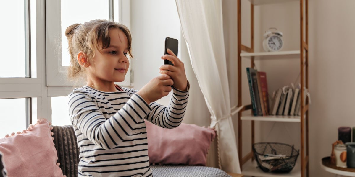 Young girl sitting on couch holding up a phone 