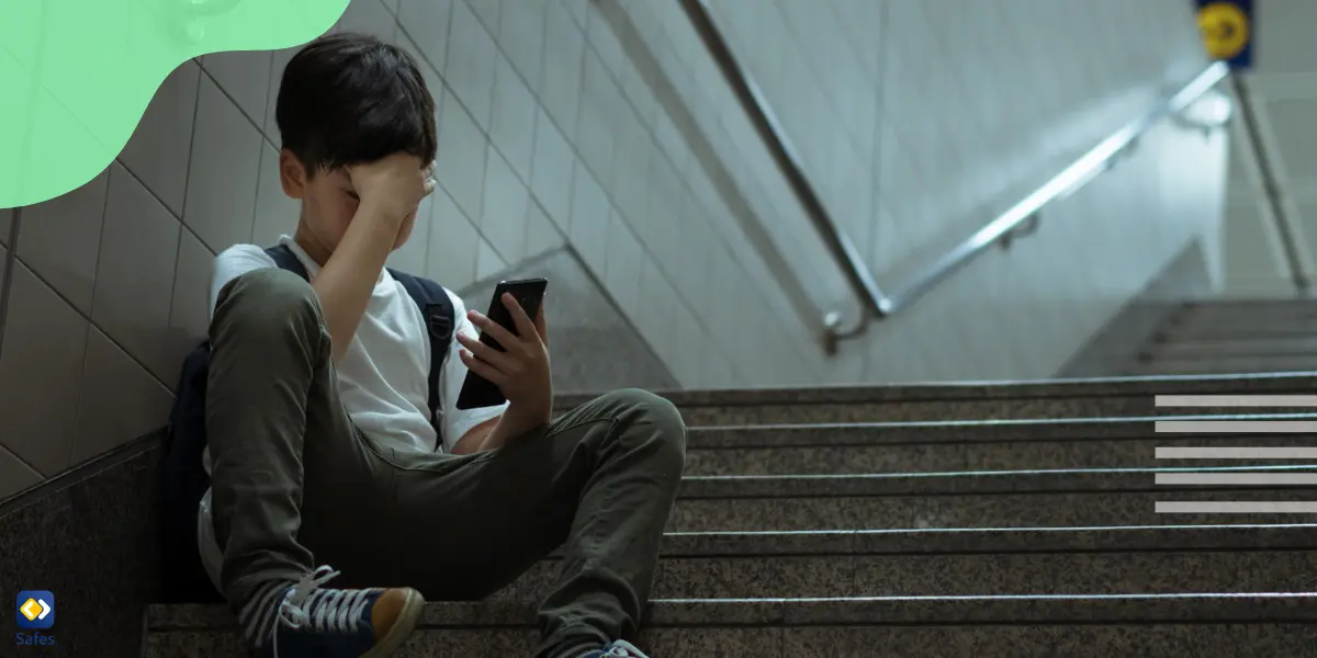 Little boy suffering from different types of cyberbullying is looking at his phone while trying to cover his face