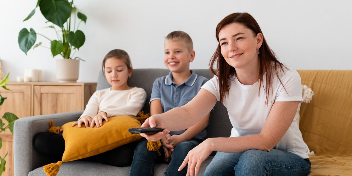 A mother and her two sons watching TV on a gray couch