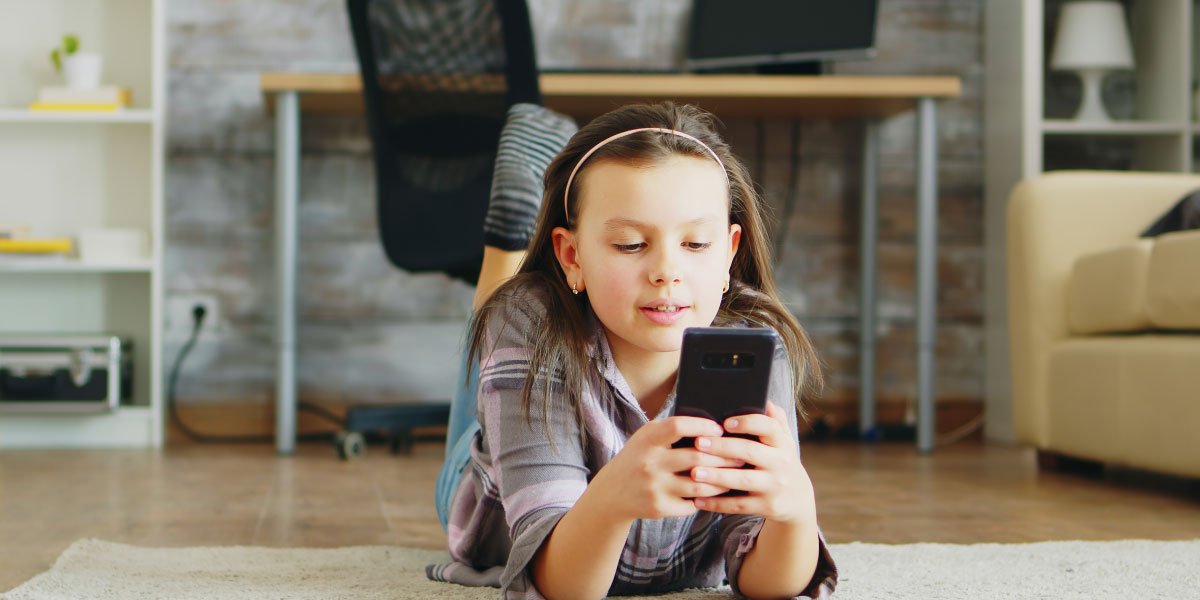 Ein Mädchen liegt auf dem Boden und benutzt ihr Smartphone 