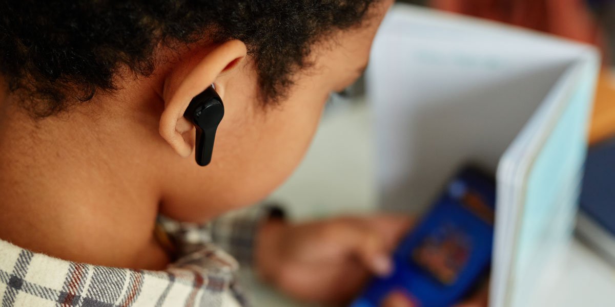 A child with headphones hiding an app on his phone