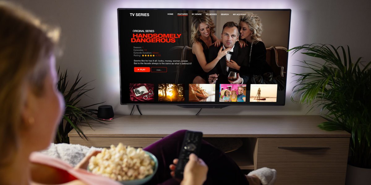 Teenage girl with a bowl of popcorn and remote control in her hands, sitting in front of the TV, which is showing the Handsomely Dangerous show details page on Netflix