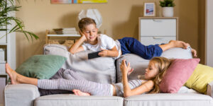 Little boy and girl on a sofa each watching their own devices