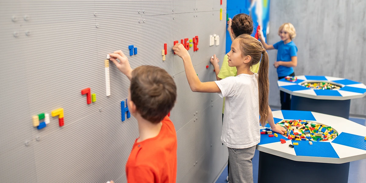 Kinder stehen in der Nähe einer Wand und machen ein Lego-Mosaik in einem kreativen Klassenzimmer