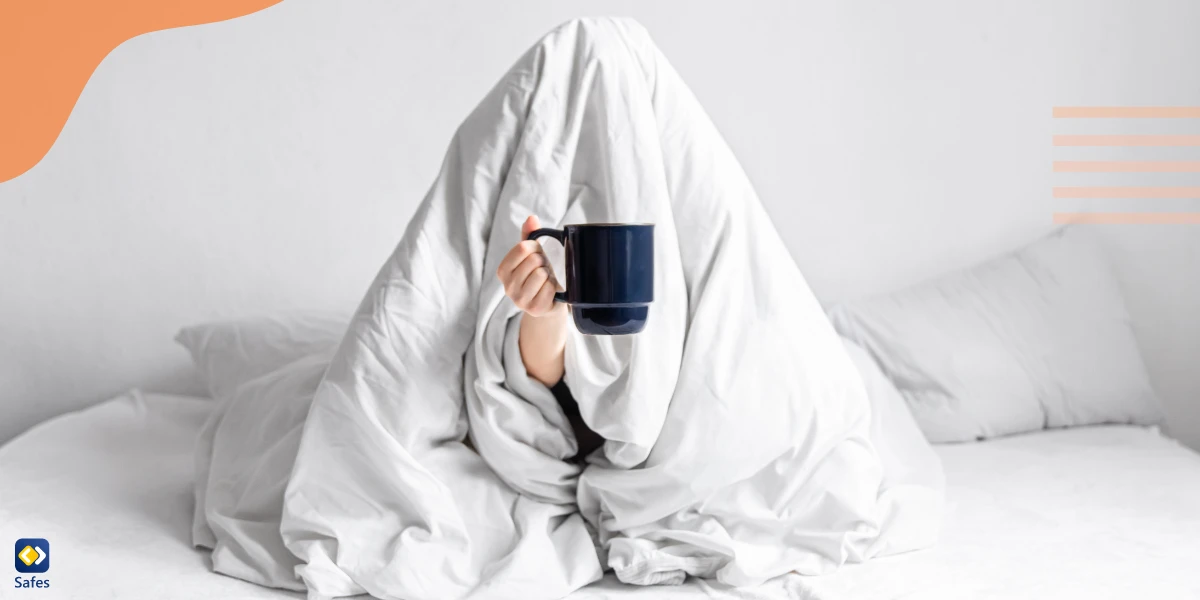 Person holding a mug under a blanket