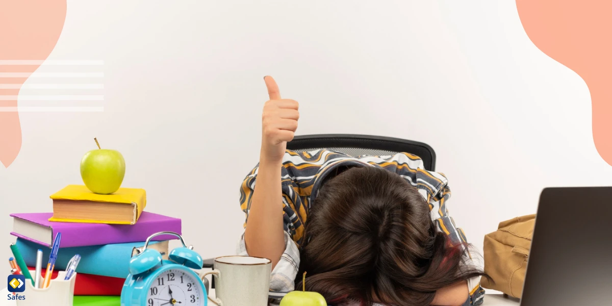 Child putting his head on his desk while holding a thumbs up