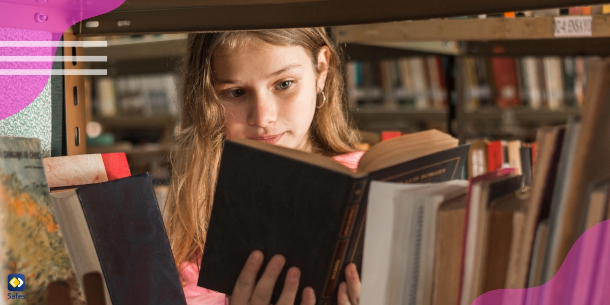 A little girl is reading a book behind a bookshelf