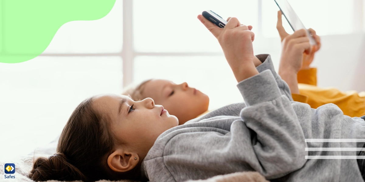 two children lying in bed, one using a phone and one using a tablet