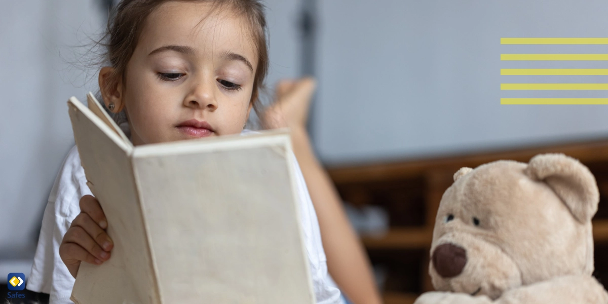 Little girl reading a book with a toy beside her