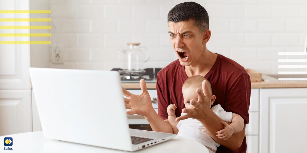 Angry man looking at laptop with a baby in his lap