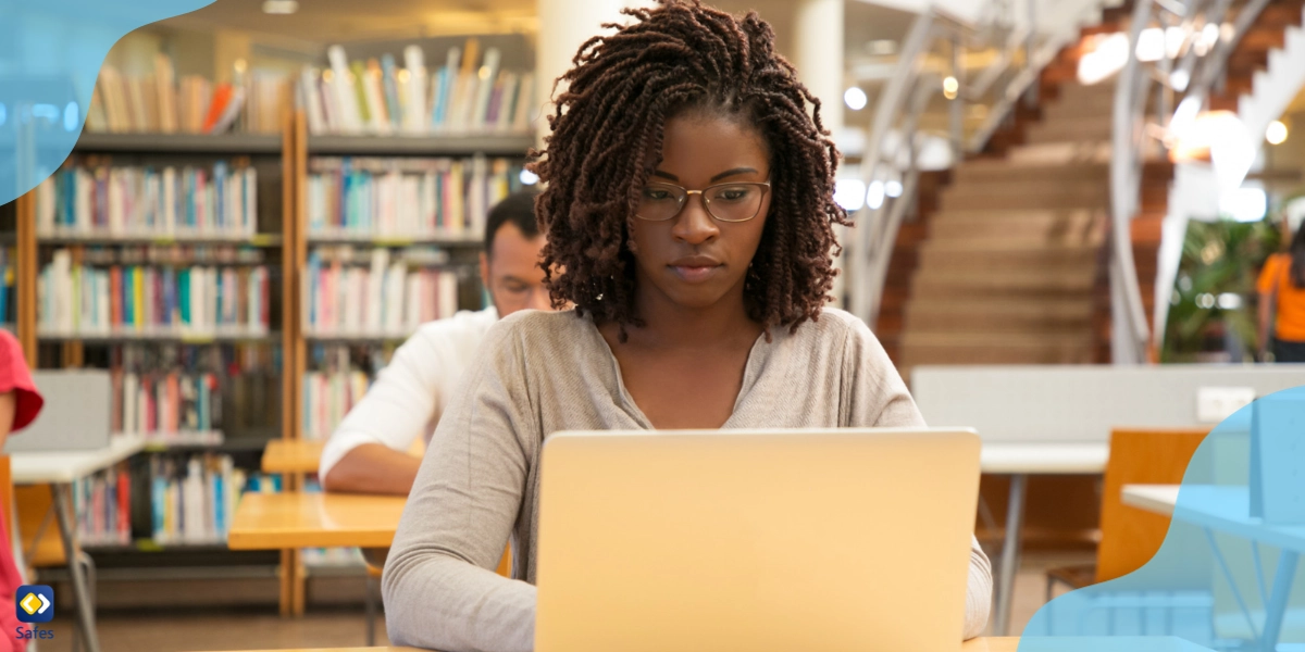 A young student in a library, studying using her laptop