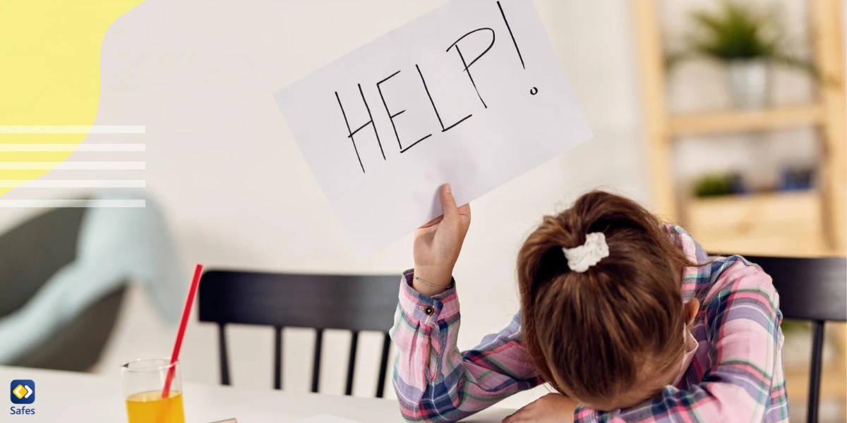 Child with head on table holding up a paper written “Help”