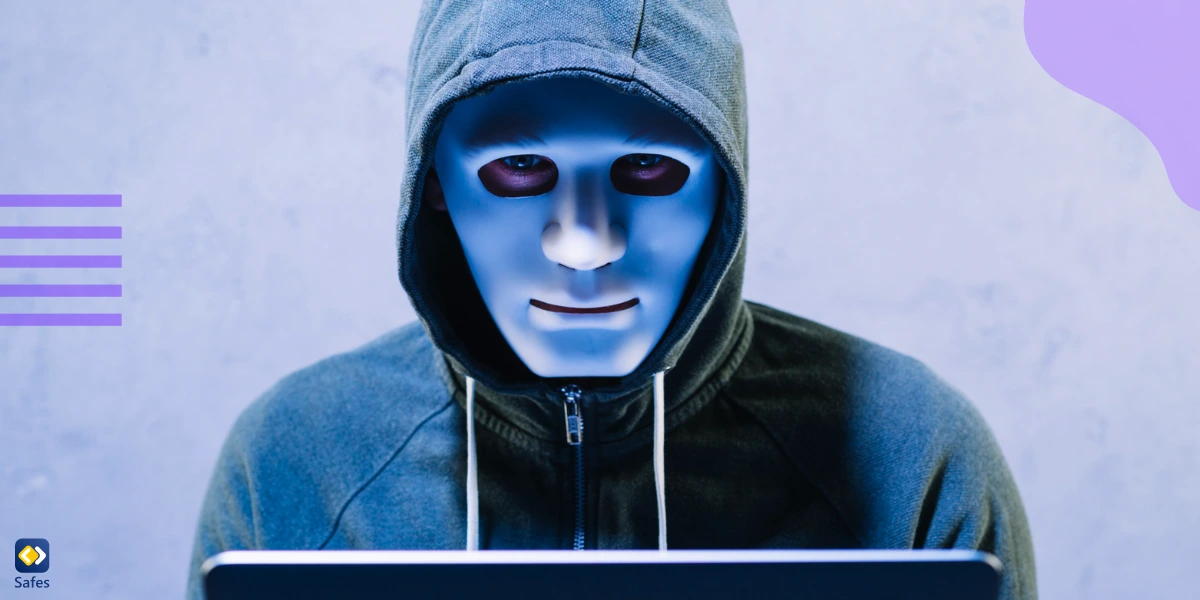 A man wearing a hoodie and a face mask, sitting behind a laptop