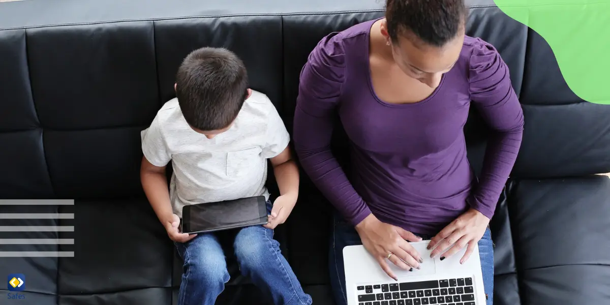 a boy is watching videos online and her mother next to her is working with a laptop resting assured that her son is not exposed to inappropriate content thanks to web filtering.