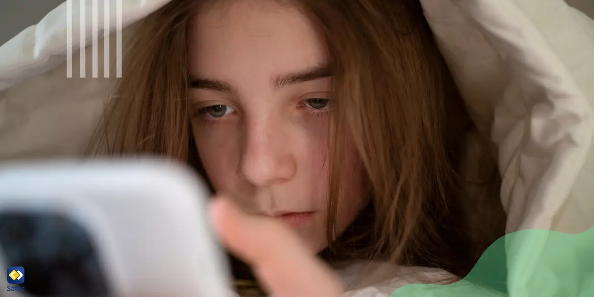 a girl on her bed and under the blanket is using her phone and being cyberbullied