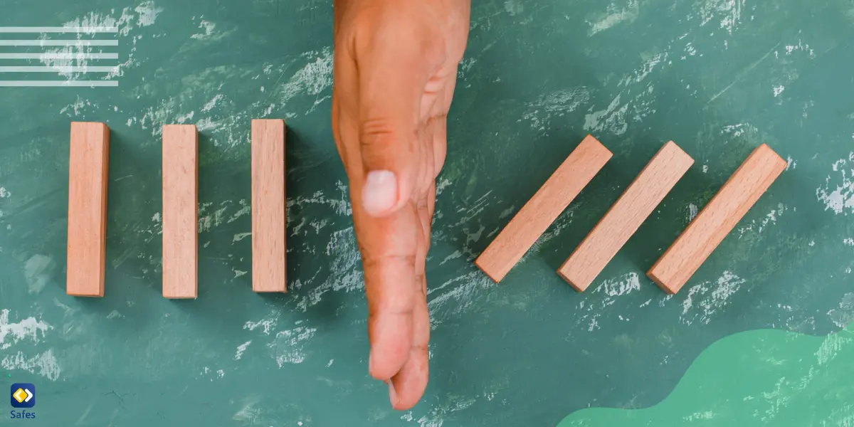 A hand is positioned as a barrier, dividing wooden blocks on a surface, symbolizing the concept of setting boundaries and creating separation or protection.