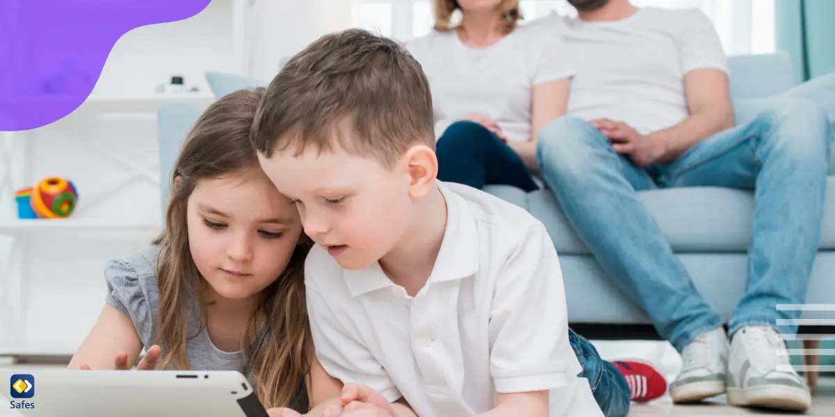 A young girl and boy are watching something on their digital device while their parents monitor their activities from behind.