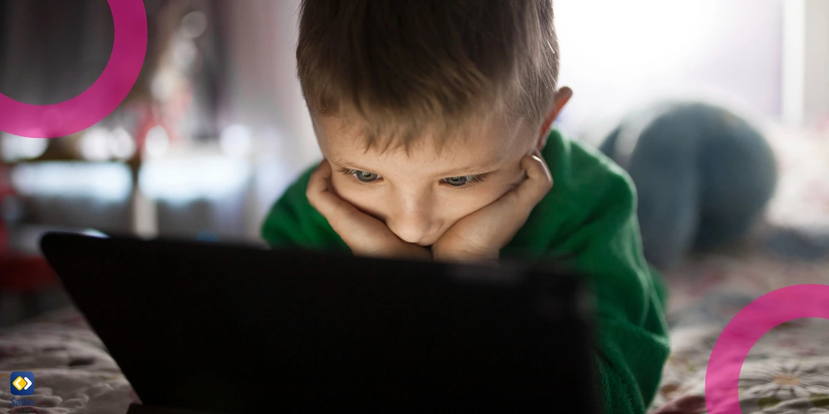 A boy laying down on a bed, watching inappropriate content on his tablet.