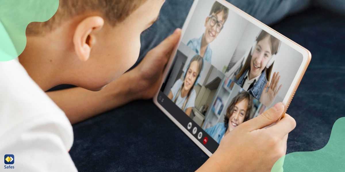 A young boy sitting, using a tablet for a Zoom video call, smiling and talking to his friends in a home environment.