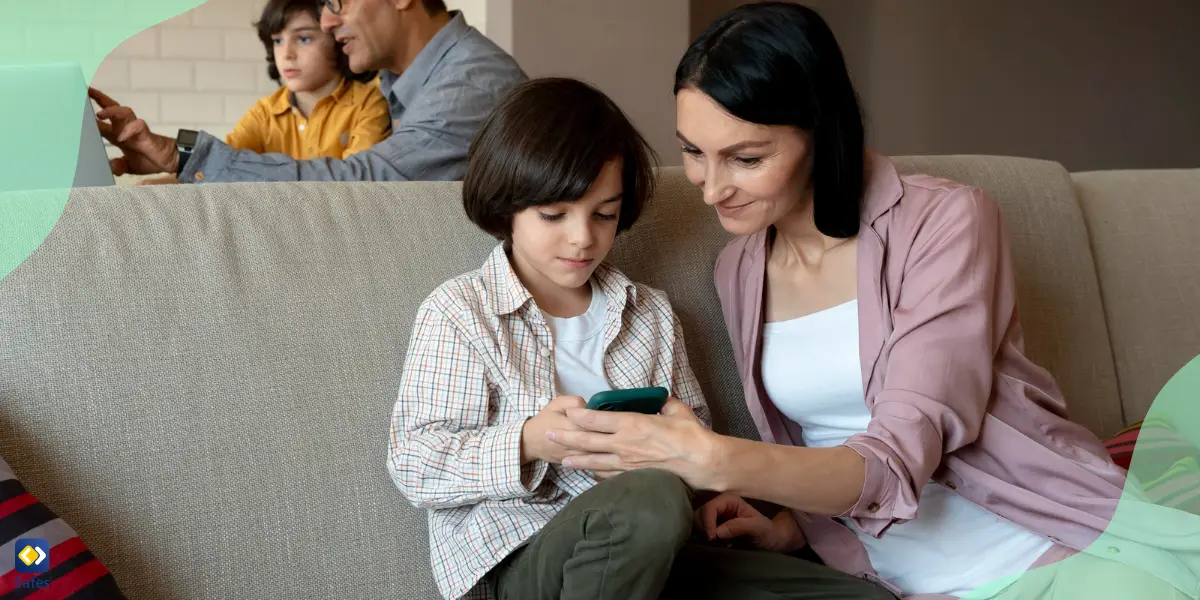 Mutter und Sohn schauen gemeinsam auf das iPhone, im Hintergrund benutzen Vater und Sohn den Laptop