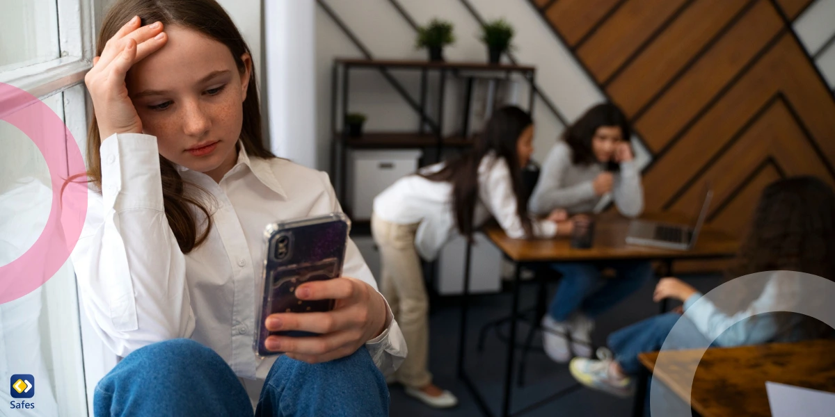 teen girl using her phone and sitting separate from a group of girls talking