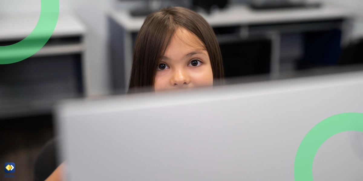 A young girl peers over a computer screen.