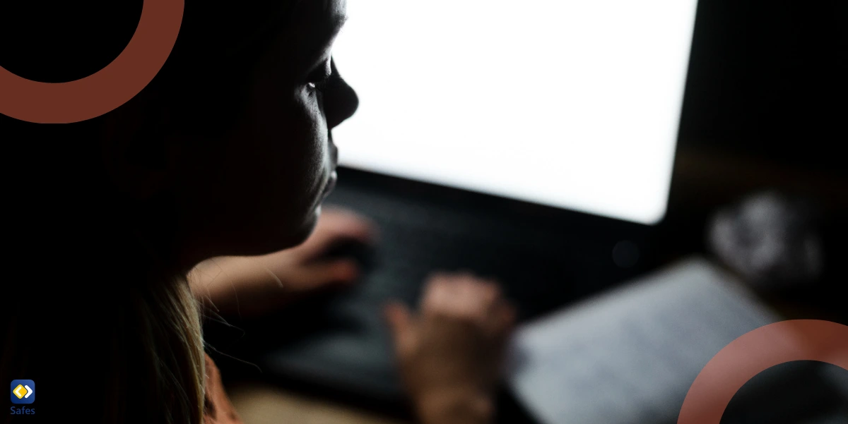 A girl working on a laptop in a dark environment, with her face illuminated by the bright screen.