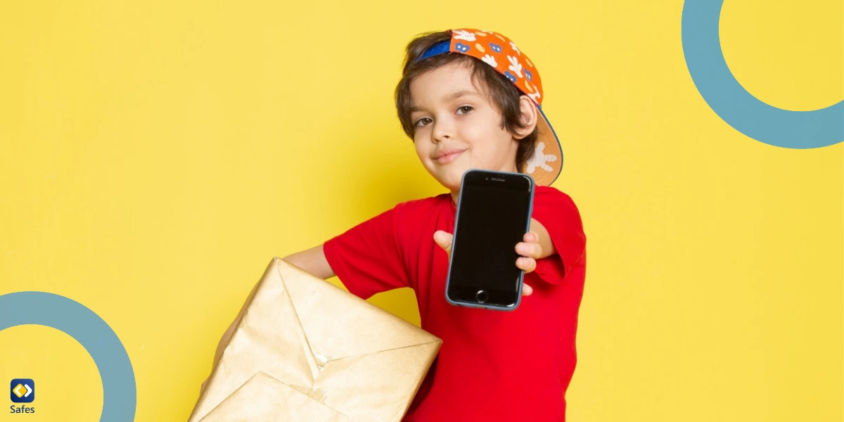 A young boy in a red t-shirt and a colorful cap poses against a bright yellow background. He holds a wrapped gift box in one hand and a smartphone in the other.