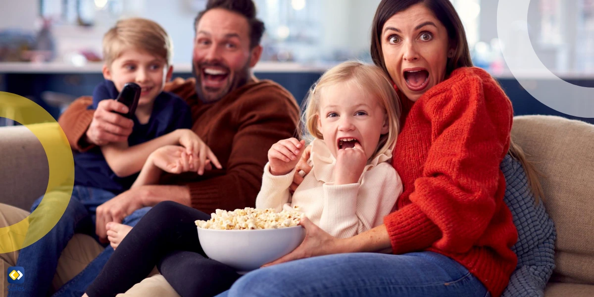 family of four watching tv with mother and daughter being scared while father and son are smiling