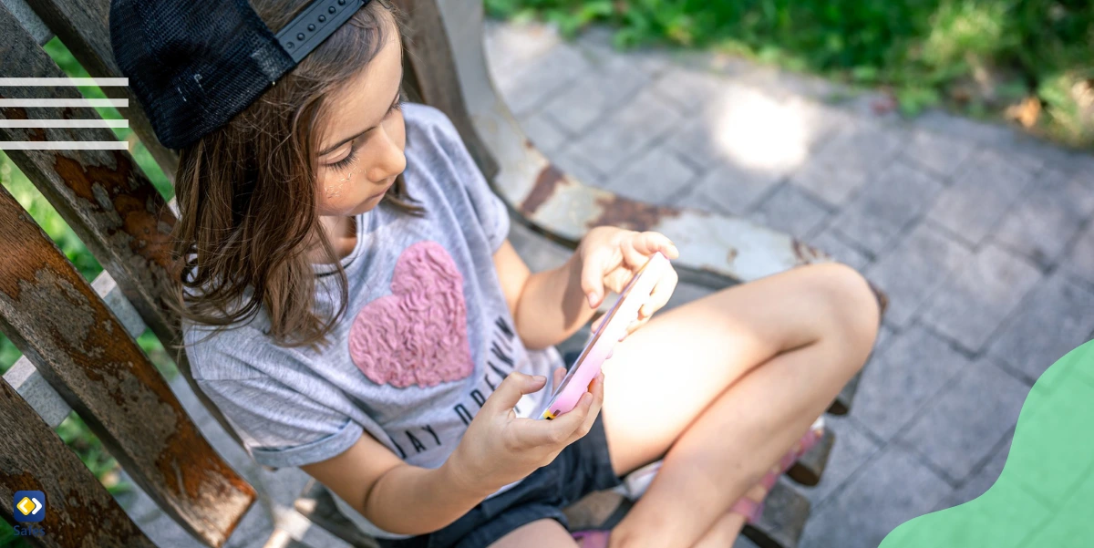 Ein junges Mädchen sitzt im Sommer auf einer Holzbank im Freien und ist in ihr Smartphone vertieft.