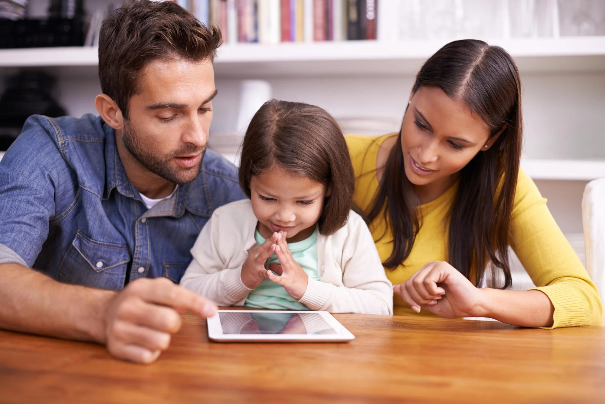 parents and child sitting at a table watching a tablet