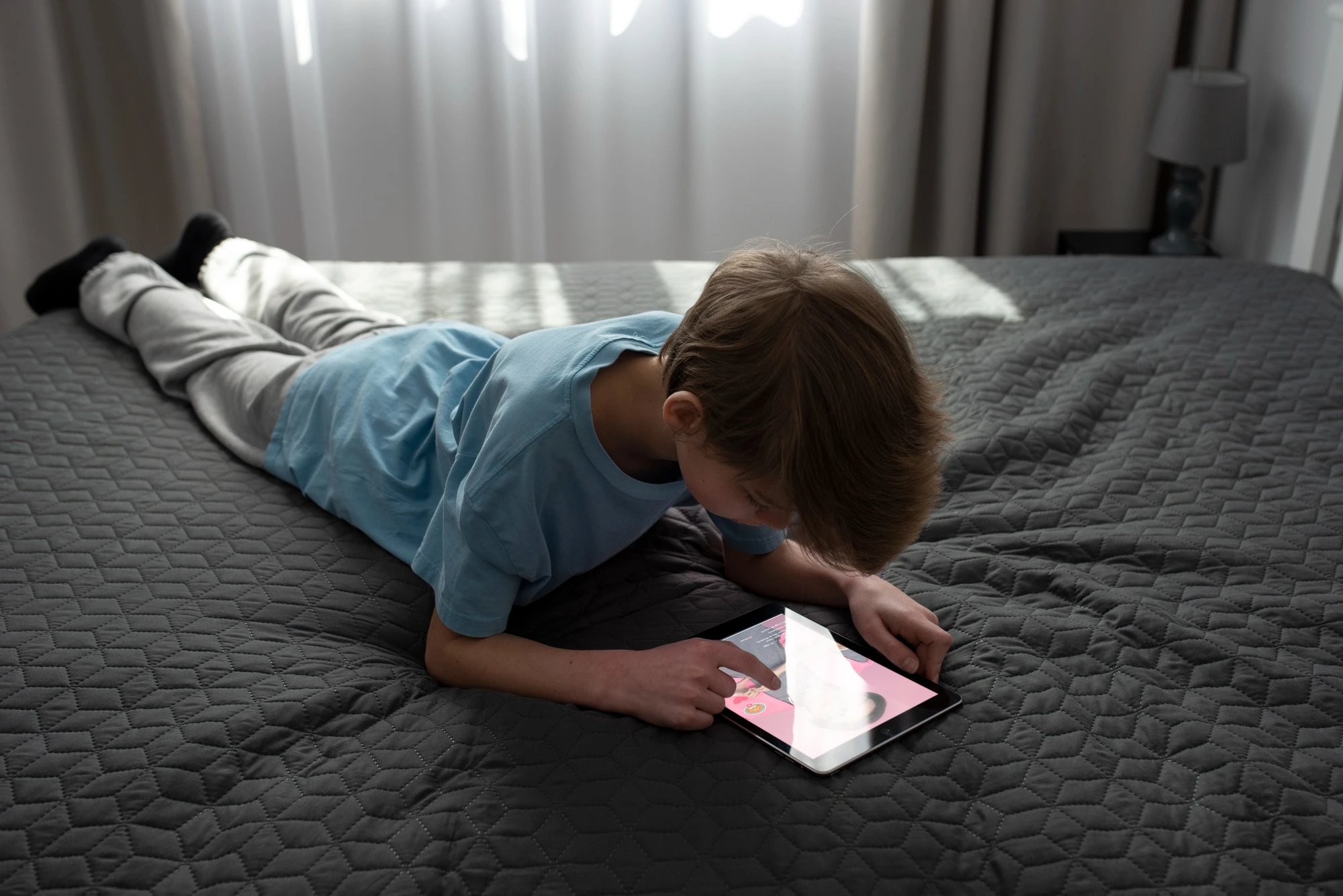 boy laying on bed and watching videos on his tablet