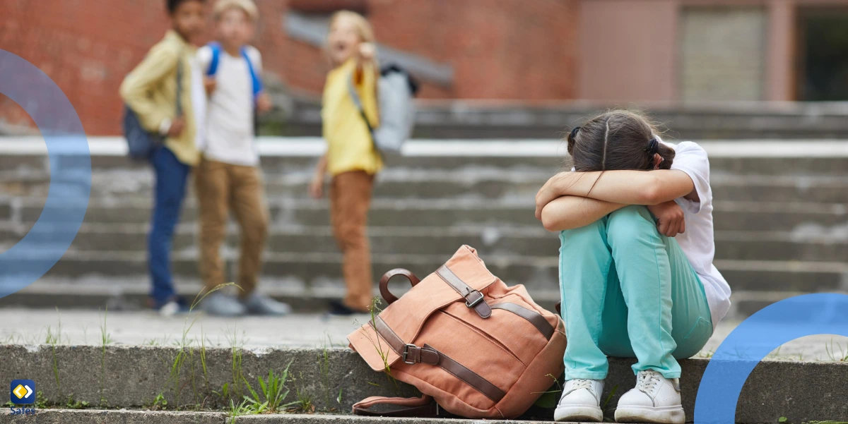 a crying schoolgirl sitting on stairs outdoors with group of teasing children bullying her in the background